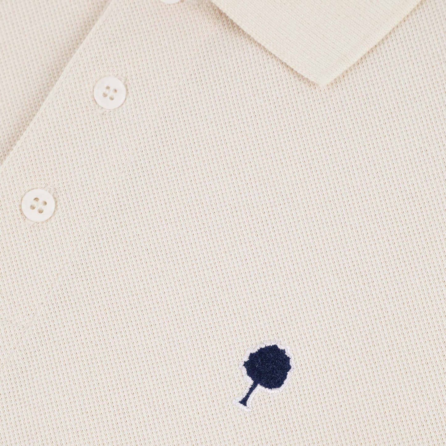 Zoom sur le logo brodé du polo piqué écru FAGUO en coton recyclé