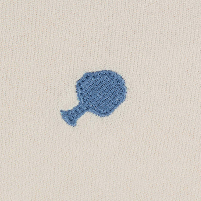 Zoom sur le t-shirt écru FAGUO avec le logo bleu brodé, détail poitrine
